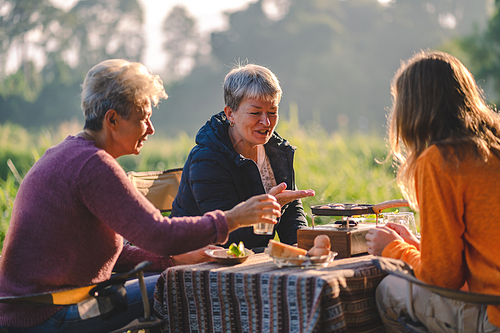 woman family having fun with food of picnic camp in the nature morning, summer travel vacation lifestyle of mother and girl at adventure forest park landscape in holiday, outdoors activity breakfast