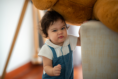 Cute little toddler girl holding circular cookie toy while sitting on floor with stuff toy in living room playing with young father at home