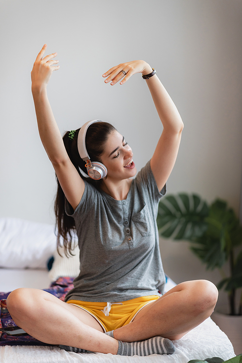 Portrait of young and carefree young woman in casual clothing listening to music using wireless bluetooth headphones dancing and enjoying at home with eyes closed and relaxing