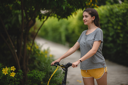 Carefree and young cheerful woman relaxing and enjoying while exercising on cycle outdoor in lane surrounded by greenery plants on a summer morning
