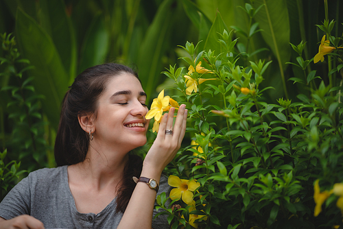 Beautiful young woman with toothy smile feeling and smelling beautiful yellow flower while in nature enjoying and relaxing with closed eyes