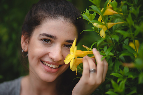 Beautiful young woman with toothy smile feeling and smelling beautiful yellow flower while in nature enjoying and relaxing with closed eyes