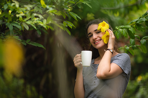 Cheerful and beautiful young carefree woman relaxing and breathing fresh air while sitting in balcony with nature view and drinking morning coffee and beverage and looking at scenic view