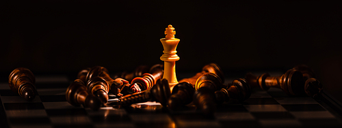 Close-up leader chess piece standing with falling silver pawn chess pieces on chessboard on dark background. Leadership and winner competition or business success teamwork strategy concept