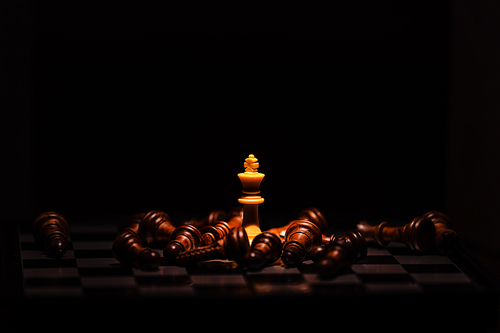 Close-up leader chess piece standing with falling silver pawn chess pieces on chessboard on dark background. Leadership and winner competition or business success teamwork strategy concept