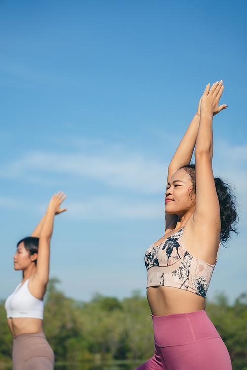 Group of people doing yoga exercises by the lake at morning outdoor, Woman practicing yoga in lotus position at park, Multinational women doing breathing exercises or yoga meditation during outdoor