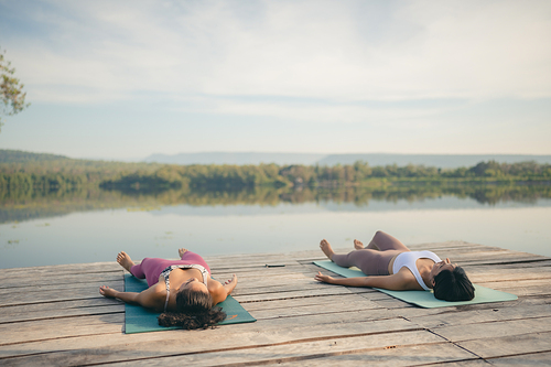 Group of people doing yoga exercises by the lake at morning outdoor, Woman practicing yoga in lotus position at park, Multinational women doing breathing exercises or yoga meditation during outdoor