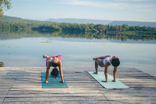 Group of people doing yoga exercises by the lake at morning outdoor, Woman practicing yoga in lotus position at park, Multinational women doing breathing exercises or yoga meditation during outdoor