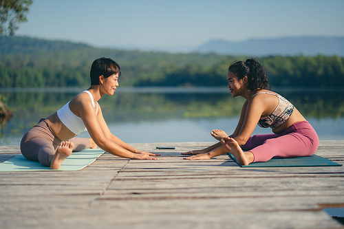 Group of people doing yoga exercises by the lake at morning outdoor, Woman practicing yoga in lotus position at park, Multinational women doing breathing exercises or yoga meditation during outdoor