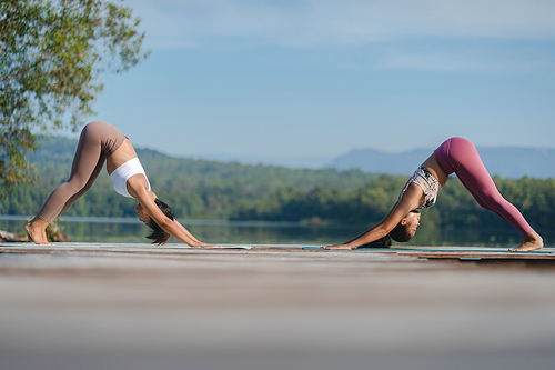 Group of people doing yoga exercises by the lake at morning outdoor, Woman practicing yoga in lotus position at park, Multinational women doing breathing exercises or yoga meditation during outdoor