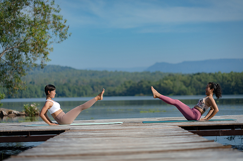 Group of people doing yoga exercises by the lake at morning outdoor, Woman practicing yoga in lotus position at park, Multinational women doing breathing exercises or yoga meditation during outdoor