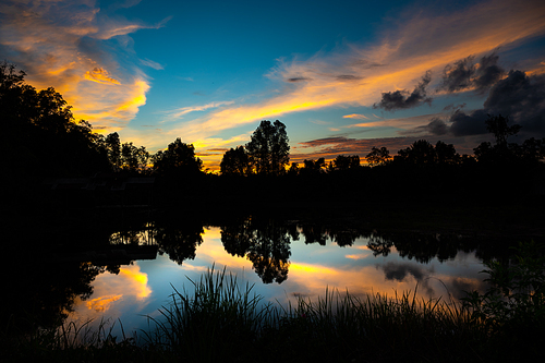 A beautiful sunset evening with blue and orange cloudy sky against a forest scenery near a lake with reflection and no people around
