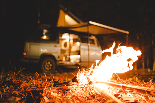 camping concept with camper van and fire at night under the tree in the forest mountain field