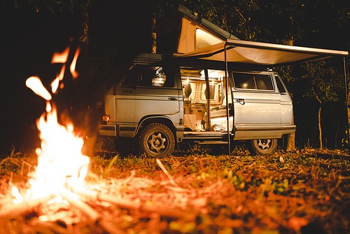 camping concept with camper van and fire at night under the tree in the forest mountain field