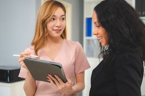 Young Asian female business woman and manager showing presentation and feedback to employee on digital tablet holding a digital pen while in conversation at a modern office