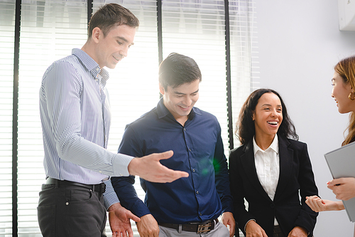 Group of young Asian and multiethnic business man and business woman standing while having a friendly conversation and discussion during break time in modern office