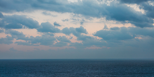 짙은 구름으로 뒤덮힌 흐린 하늘의 새벽 바다 풍경.
