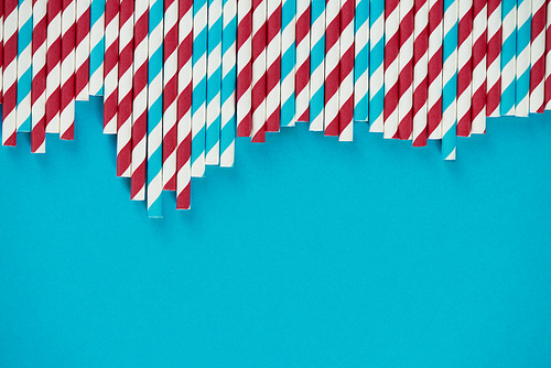 Directly above view of colorful drinking straws lying on turquoise surface, their ends forming uneven line
