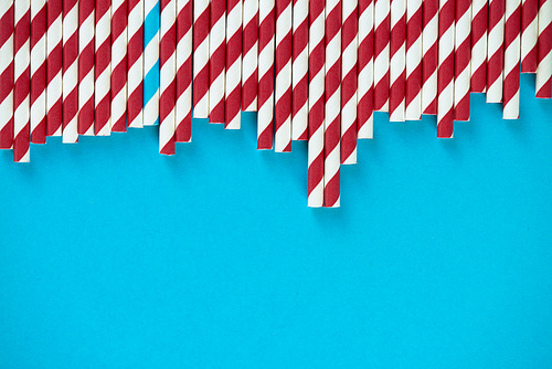 Drinking straws with deep red and white stripes lying in a row against turquoise background, one with blue stripes mixed in with them