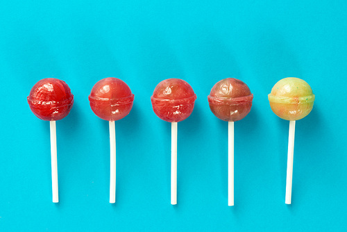 Directly above view of five appetizing lollipops lying in a line against turquoise background