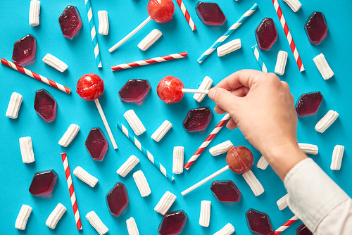 Process of colorful composition creation: unrecognizable man setting out appetizing sweets and colorful drinking straws in a certain order, directly above view