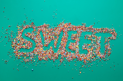 Sweet inscription written on colorful sprinkles, green background