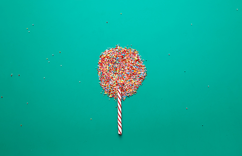 Lollipop made of sprinkles and candy cane on green background, sweets concept