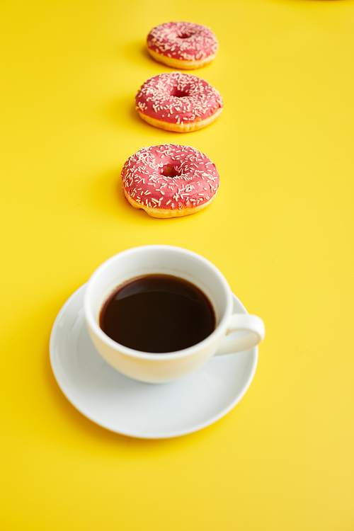 Ceramic cup of black coffee and sweet doughnuts in row on yellow background