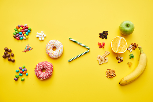 Comparing candies and fruits: greater-than sign between heap of various sweets and fresh and dried fruits