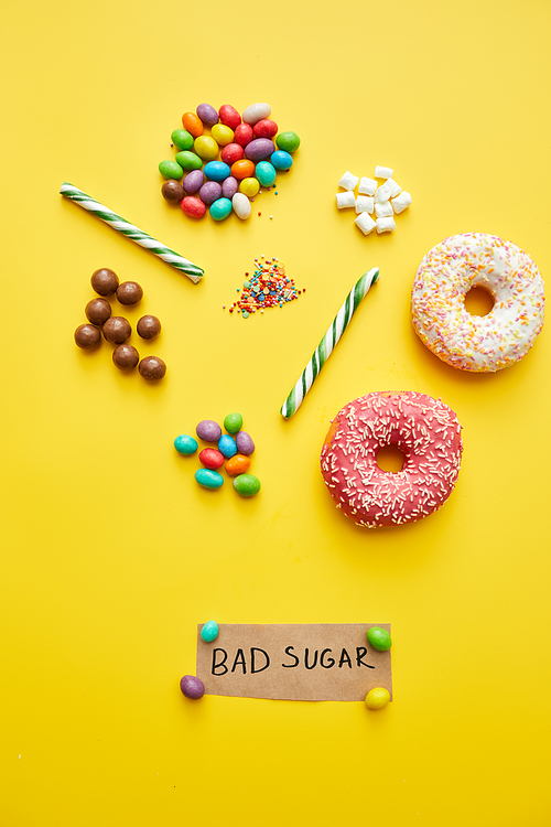 Bad sugar concept: various unhealthy sweets such as doughnuts, jellybeans and candy canes on yellow background