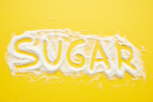 Sugar word written on granulated sugar, yellow background