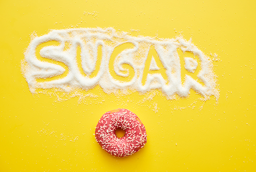 High angle view of sugar inscription written on powder and delicious doughnut with topping on yellow background