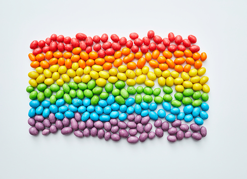 Multi-colored candies laid out in shape of equality flag on white background, sweet food and creativity concept