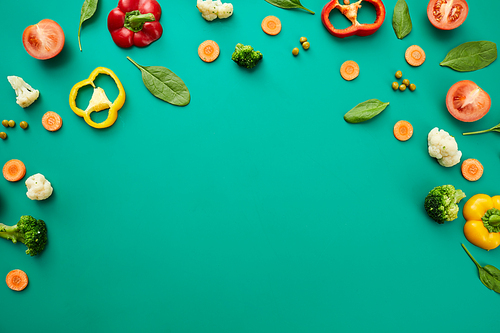 Various fresh vegetables such as tomato, broccoli, peas, bell pepper and leaves on green background