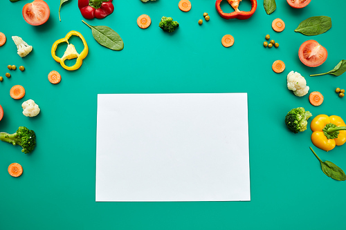 Chopped healthy vegetables and leaves with blank white paper sheet on green background
