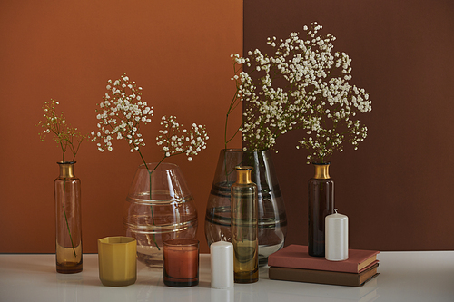 Beautiful aromatic still life composition with flowers in glass vessels and perfume candles on brown background