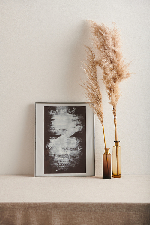 Modern still life shot of abstract black and white painting in frame with and dried plant branches in glass vessels against white wall background