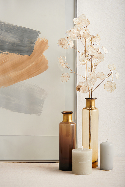 Modern still life composition shot of lunaria flowers, glass vessels and abstract painting against white wall background