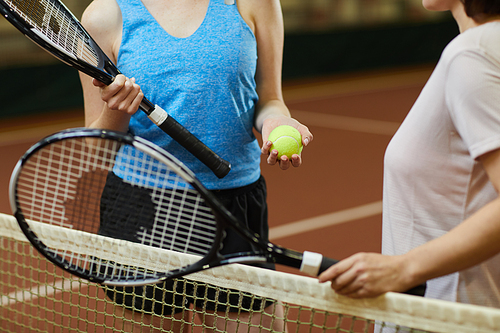 Close-up of unrecognizable women with racquets standing at tennis net and choosing who will pitch tennis ball