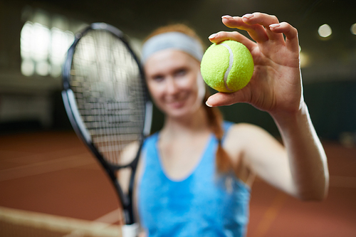 Close-up of female player standing on court and showing green tennis ball, focus on ball in hand