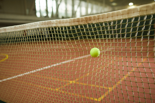 Close-up of green tennis ball hitting to net considered as out on indoor court, background of tennis game