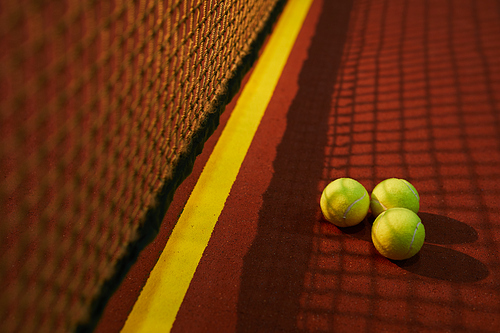 Close-up of three yellow tennis balls placed in shadow of net on court, tennis game concept