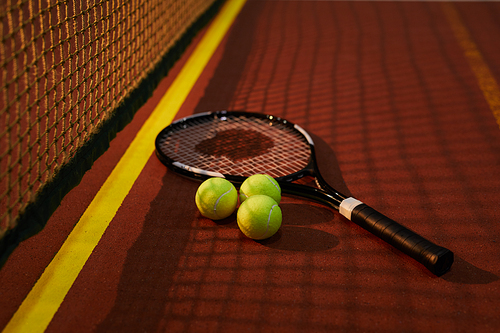 Background of tennis racket with three green balls in shadow of tennis net on court floor, recreational game concept