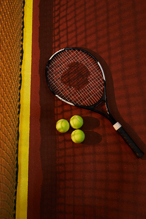 Above view of tennis equipment such as racket and balls lying near net on court floor, sport and hobby concept