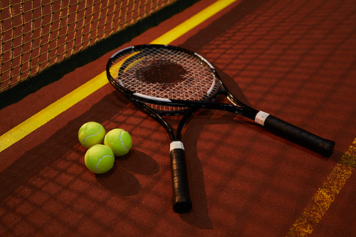 Close-up of tennis racquets of competitors and tree tennis balls lying in shadow of net on court, recreational game concept