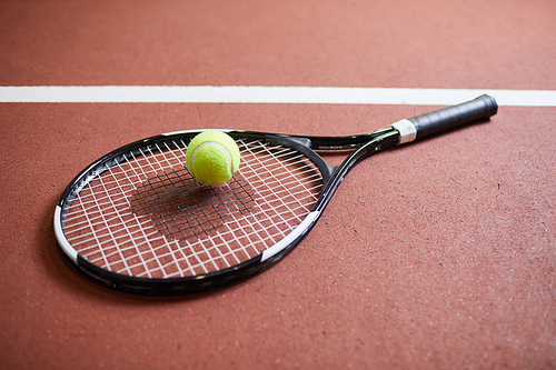 Close-up of tennis player equipment such as racket and ball placed on red stadium floor, tennis game concept