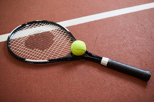 Close-up of tennis racquet and green ball placed on red floor of tennis court, copy space