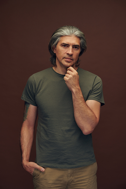 Portrait of serious mature man with gray hair standing with crossed arms against brown background