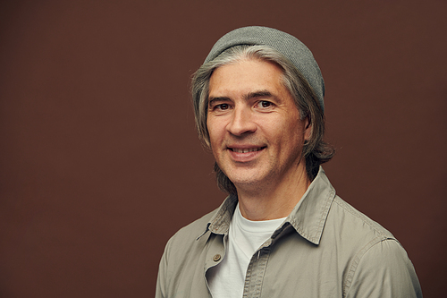 Portrait of positive confident mature manager with gray hair standing against brown background