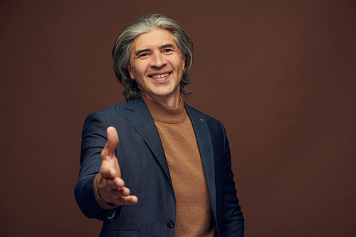 Portrait of smiling successful mature businessman with gray hairstyle reaching hand while greeting you as new business partner